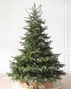 a christmas tree with presents under it on a wooden floor in front of a white wall