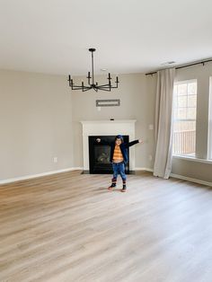 a young child standing in an empty living room with a fireplace and large windows on either side