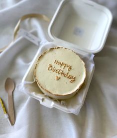 a happy birthday cake in a box on a bed with a fork and spoon next to it