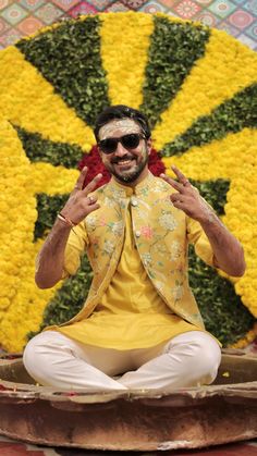 a man sitting on the ground in front of a flower display with his hands up