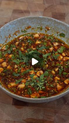 a bowl filled with beans and greens on top of a wooden table