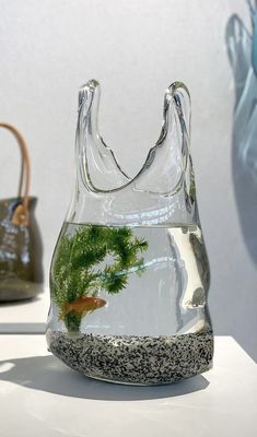 a glass vase with a fish in it on a table next to other purses