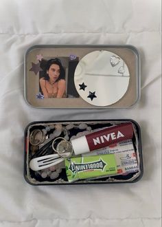 two tins filled with different items on top of a white sheet covered bed next to each other