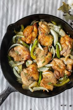 a skillet filled with chicken and onions on top of a striped table cloth next to flowers