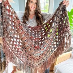 a woman is holding up a crocheted shawl