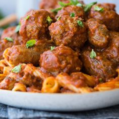 meatballs and pasta are served in a white bowl on a black tablecloth with parsley