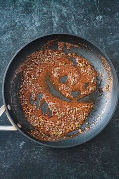 a frying pan filled with food on top of a black counter next to a wooden spoon