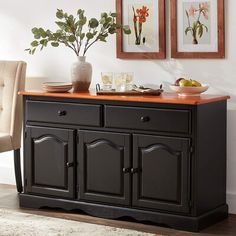 a sideboard with two vases and fruit on it in front of framed pictures