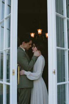 a man and woman standing next to each other in front of an open door with their arms around each other