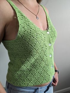 a woman wearing a green tank top with buttons on the front and back, standing in a room