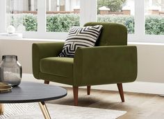 a green chair sitting in front of a window next to a table with a vase on it