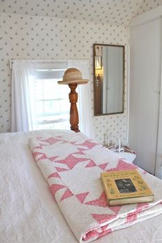 a bed with a pink and white quilt on top of it next to a mirror