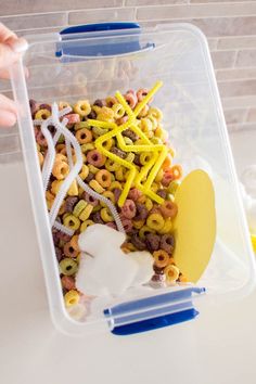 a plastic container filled with cereal sitting on top of a counter next to a person's hand