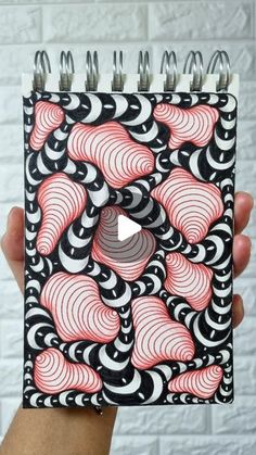 a hand holding up a spiral notebook with red and black swirls on the cover