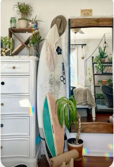 there is a surfboard leaning against the wall next to a dresser and potted plant