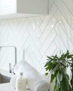 a bathroom with white tile and green plants on the counter top, next to a sink