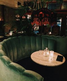 a green booth with two tables and some glasses on it in front of a chandelier