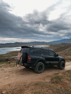 a black suv parked on top of a dirt road next to a body of water