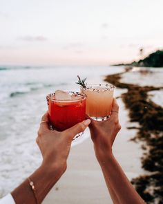 two people holding up drinks on the beach