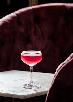 a wine glass sitting on top of a table next to a red velvet chair in front of it