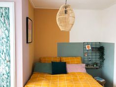 a bed with yellow sheets and pillows in a room next to a wall mounted birdcage