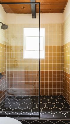 a bathroom with yellow and brown tiles on the walls, shower stall and toilet in the corner