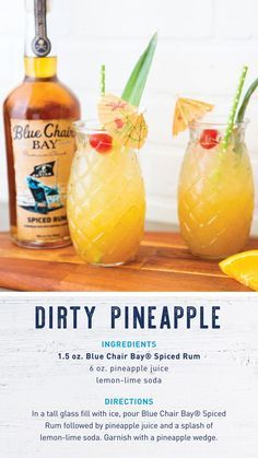 two glasses filled with pineapple drink sitting on top of a wooden table next to a bottle