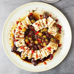 a white plate topped with sliced chicken and olives next to a bowl of sauce