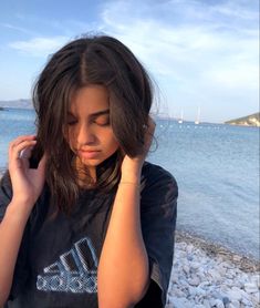 a young woman is sitting on the beach talking on her cell phone and looking down