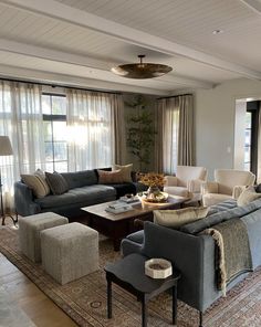 a living room filled with lots of furniture next to a window covered in sheer curtains