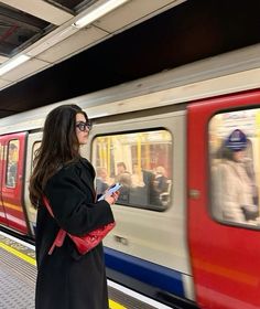 a woman standing on the platform looking at her cell phone while waiting for a train