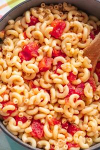 a pot filled with pasta and sauce on top of a table next to a wooden spoon