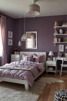 a bedroom decorated in purple and white with a bed, desk, chair, mirror and window