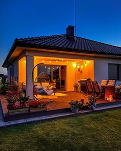 a patio with chairs and lights on it at night in front of a house that is lit up