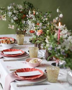 the table is set with plates, cups and vases filled with flowers on it