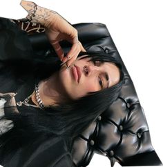 a woman with long black hair and piercings on her head sitting in a leather chair