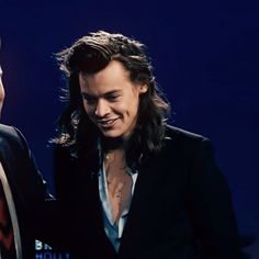 two men standing next to each other in front of a blue background and one man wearing a suit