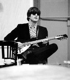 a man sitting in a chair holding a guitar and wearing a suit with polka dots on it