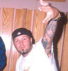 two men standing next to each other in front of a wooden wall with tattoos on their arms