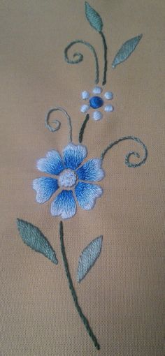 a blue flower with green leaves on a tan background is stitched onto the side of a piece of cloth