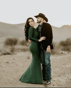 a pregnant woman in a green dress and cowboy hat standing next to a man wearing a black jacket