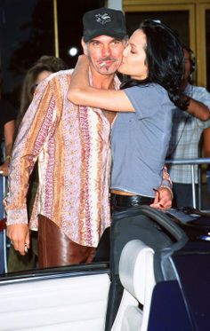 a man and woman kissing while standing next to each other in front of a car