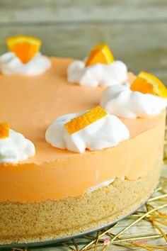 an orange cheesecake topped with whipped cream and orange slices on a gold wire cooling rack