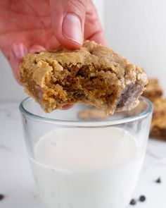 a hand holding a cookie over a glass of milk