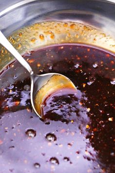 a spoon is being used to stir sauce in a large pot with brown flecks