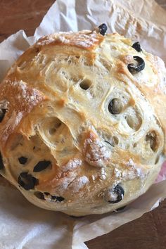 a loaf of bread with raisins and black olives sitting on wax paper