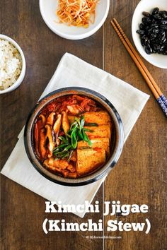 a bowl filled with food next to rice and chopsticks on top of a wooden table