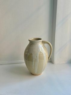 a white vase sitting on top of a table next to a window sill,