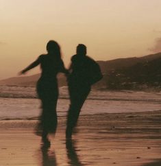 two people are walking on the beach at sunset or dawn with their hands in each other's pockets