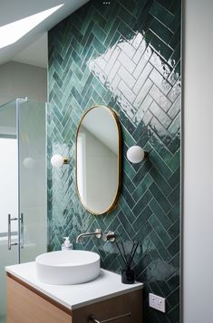 a bathroom with green tiles and a round mirror on the wall next to a sink